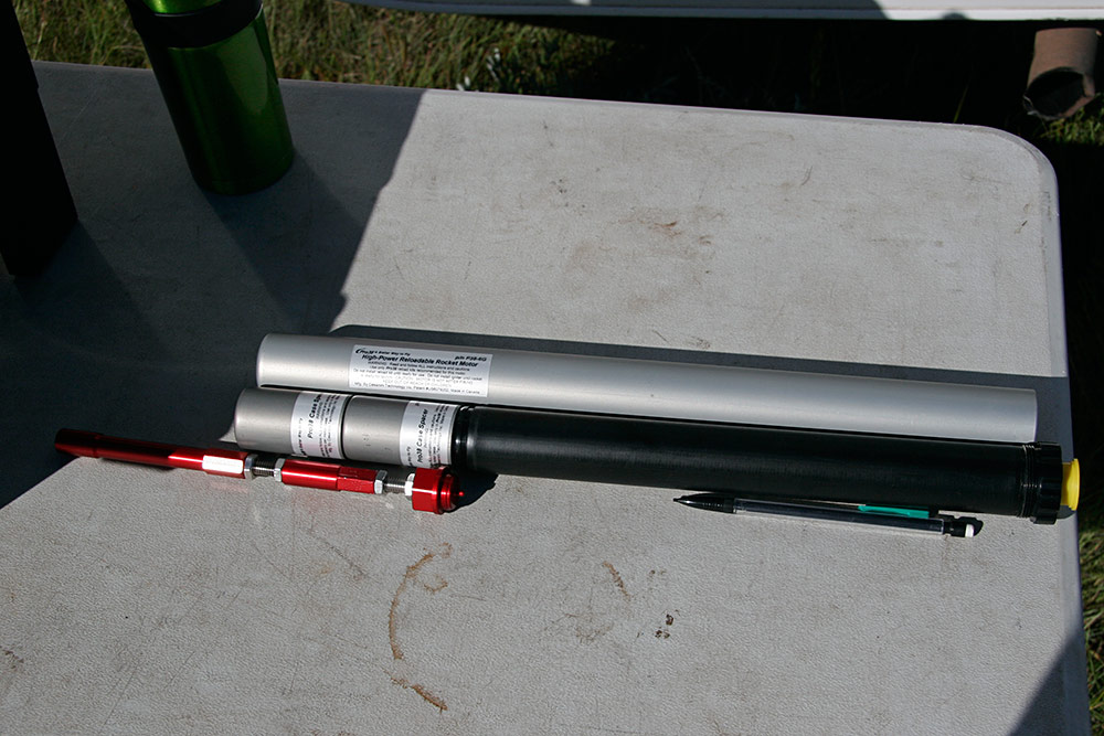 the Firestorm54 uses an adapter to hold a 38mm 6G silver casing, seen in back. <br />In the foreground is the black 4G Pro38 I470, with the two spacers in front. <br />The red motor extensions can be seen in front of the delay/eject <br />adapter which attaches to the front of the motor...